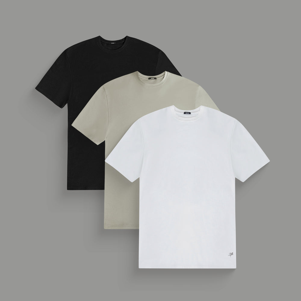 Three plain t-shirts in black, beige, and white stacked on a gray background.