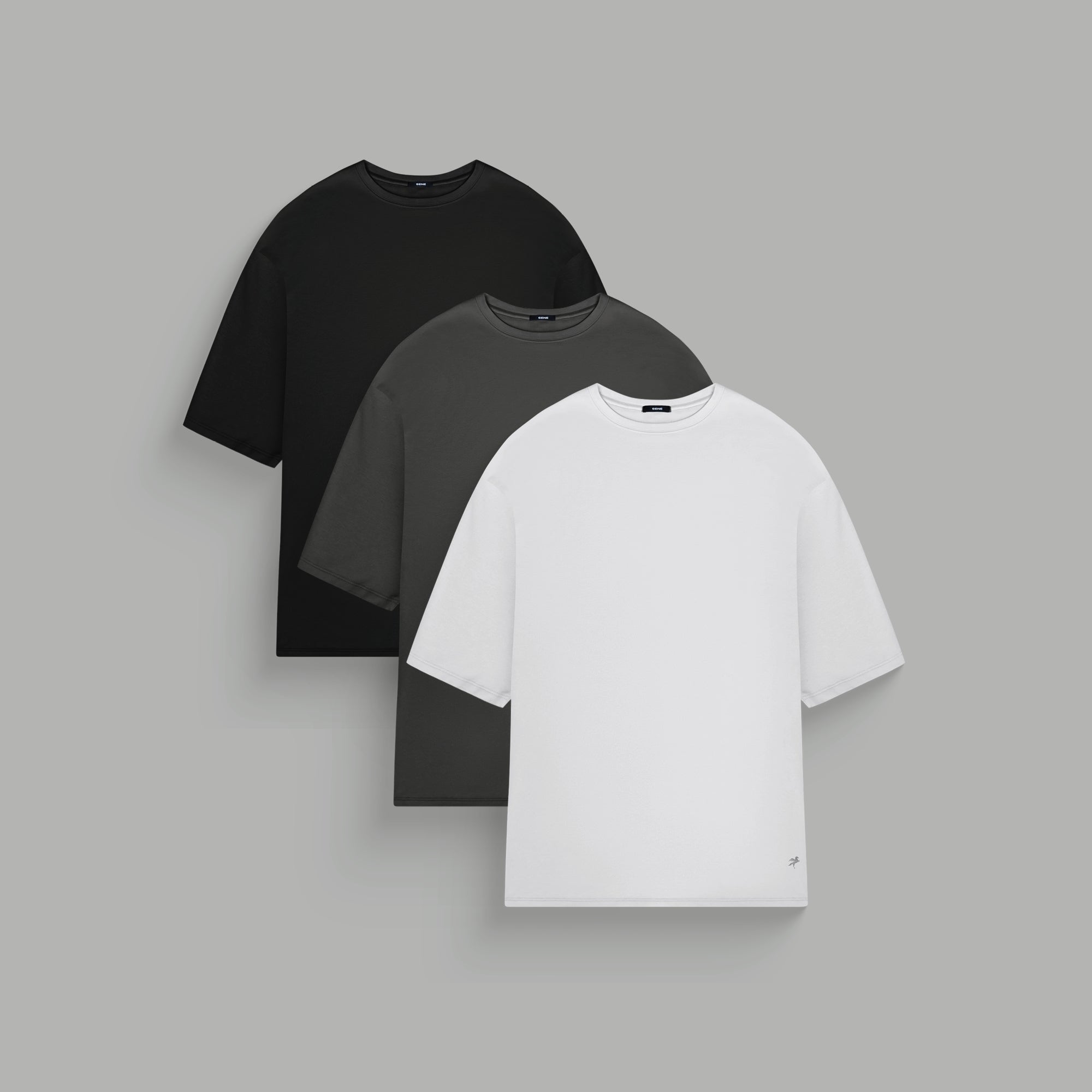 Three plain t-shirts in black, blue, and white on a gray background.