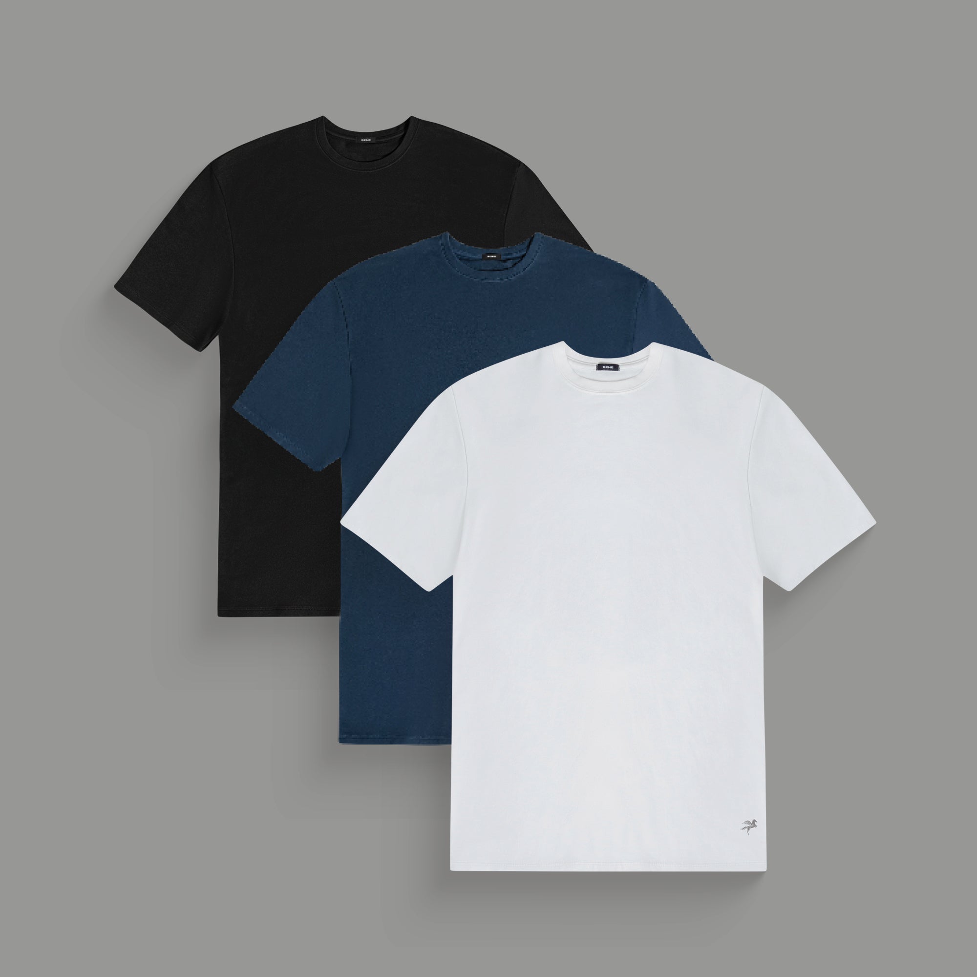 Three plain t-shirts in black, blue, and white on a gray background.