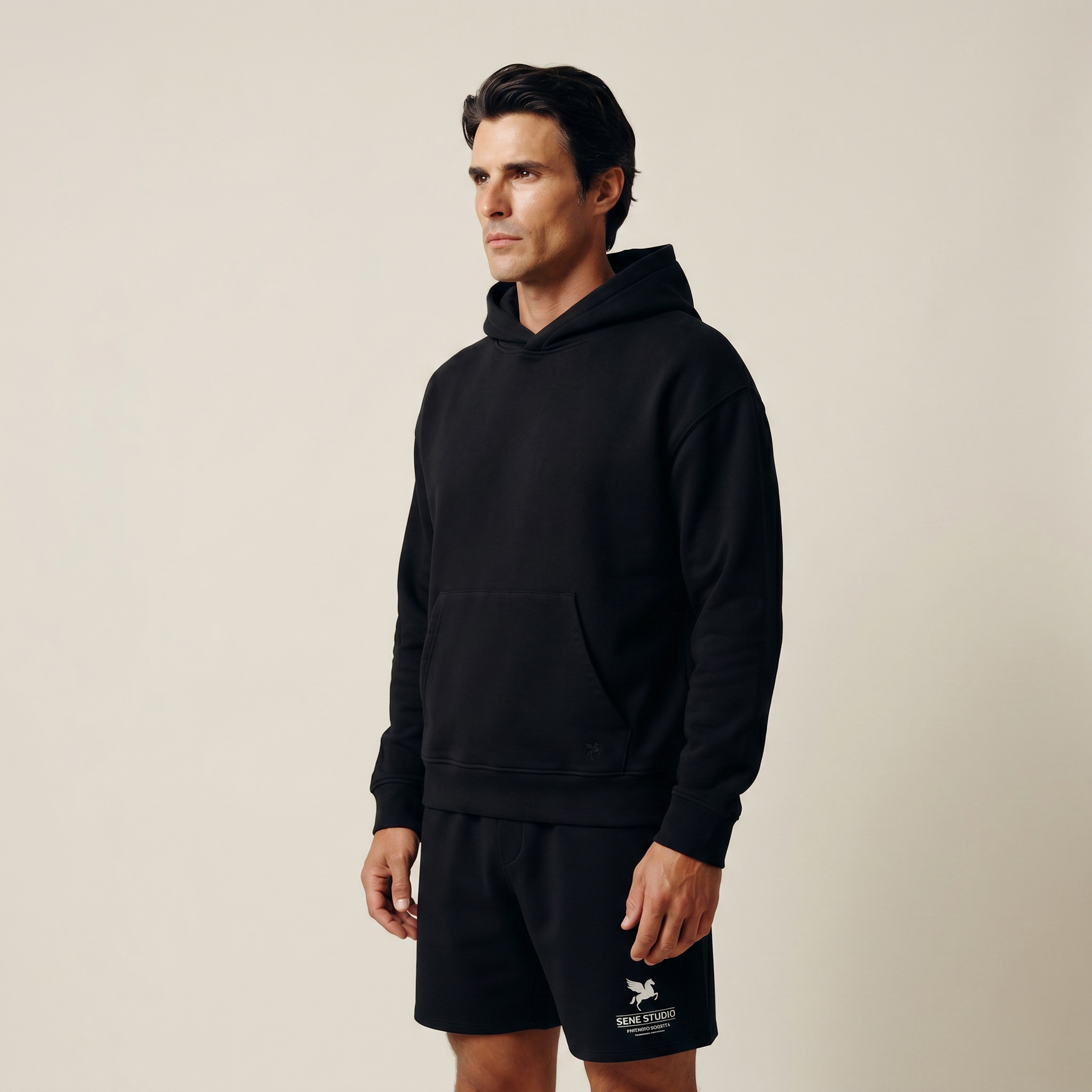 Man wearing a black hoodie and shorts with a logo on a beige background model Kive in black