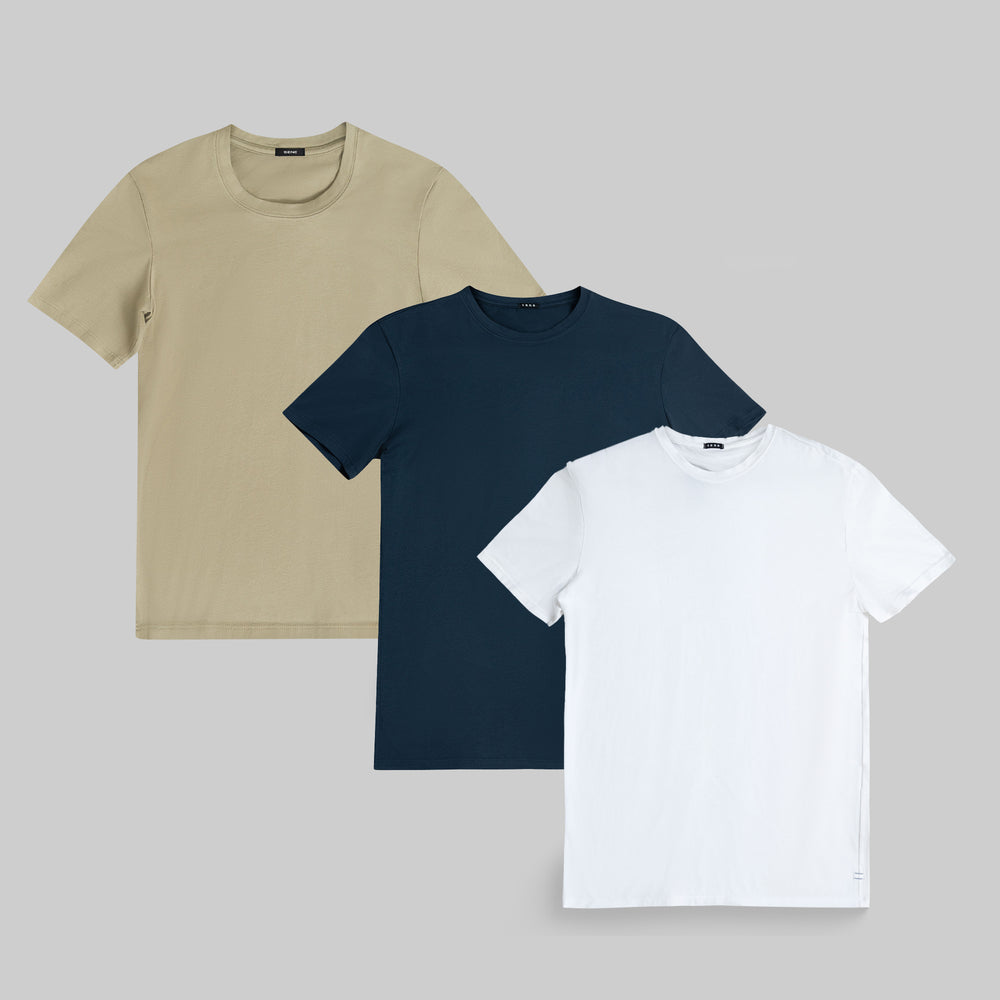 Three plain t-shirts in beige, navy, and white on a gray background.