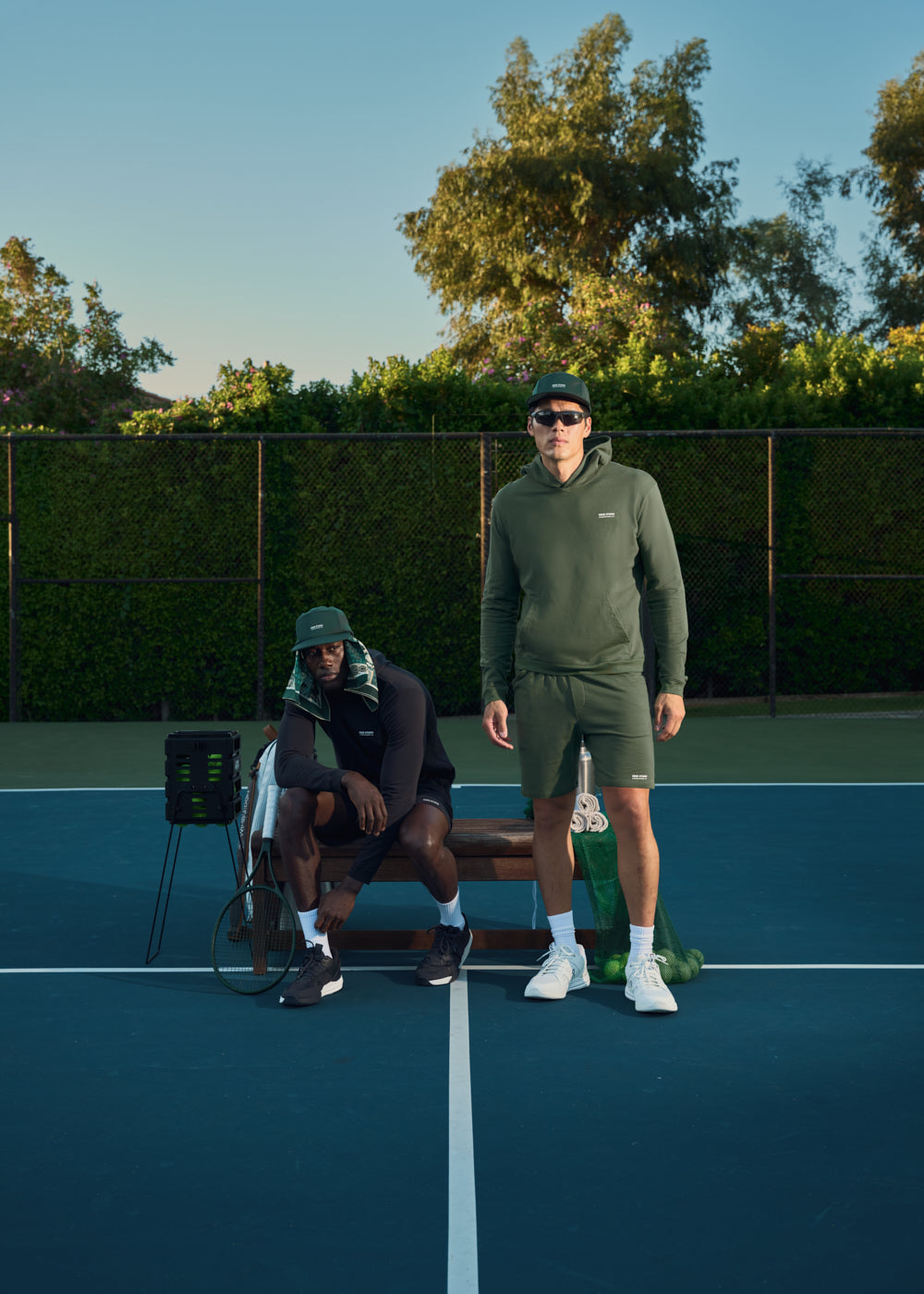 Two people in athletic wear on a tennis court, one sitting, one standing.