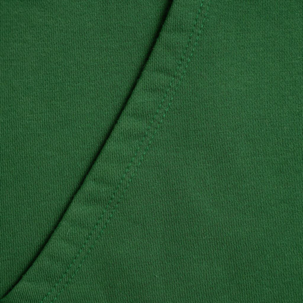 Close-up of green fabric with a visible seam Green hoodie with a brand label on a light gray background model Kive in Eden