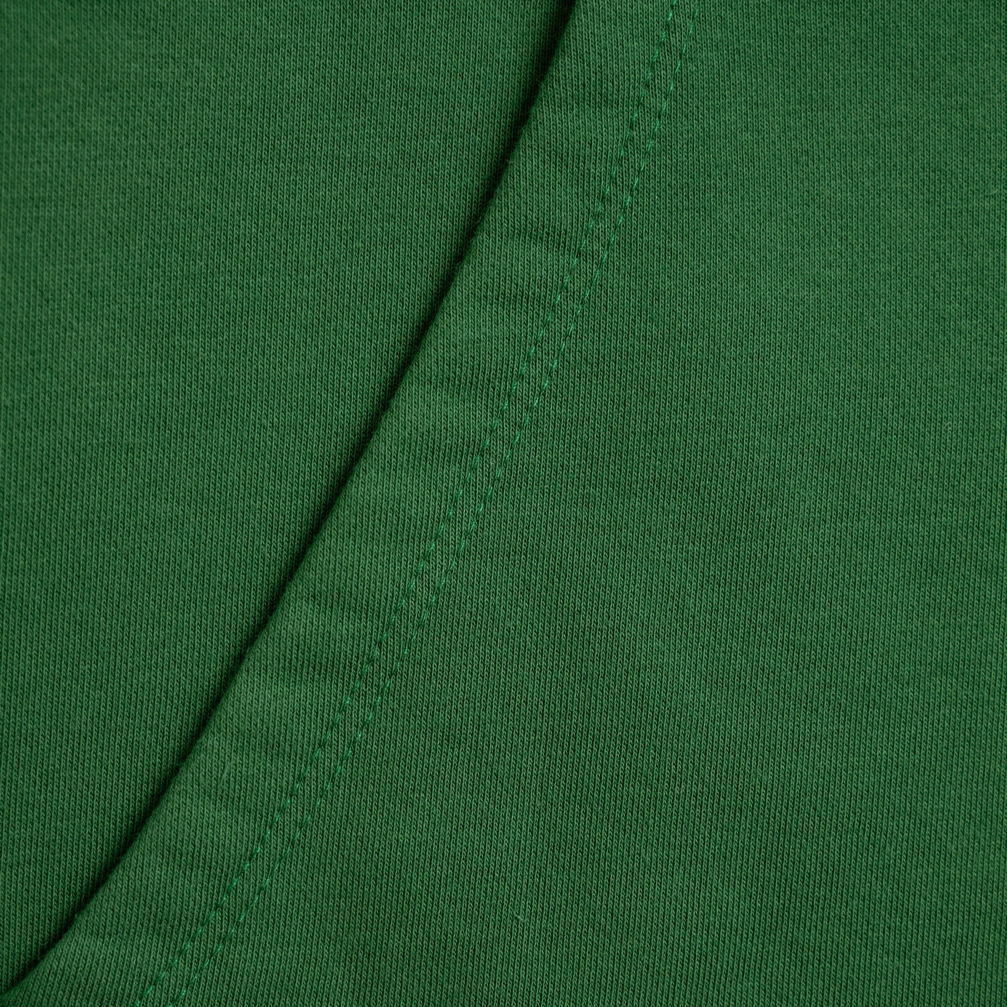 Close-up of green fabric with a visible seam Green hoodie with a brand label on a light gray background model Kive in Eden