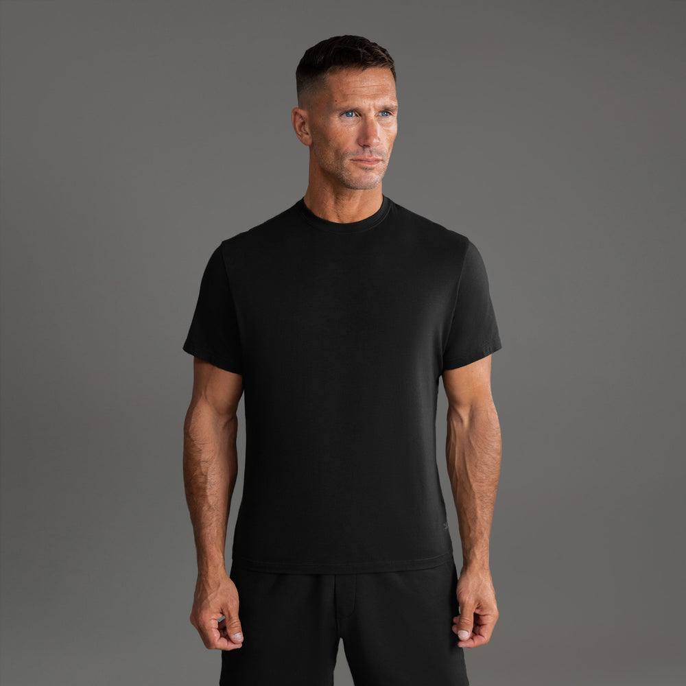 Man wearing a black t-shirt standing against a gray background.