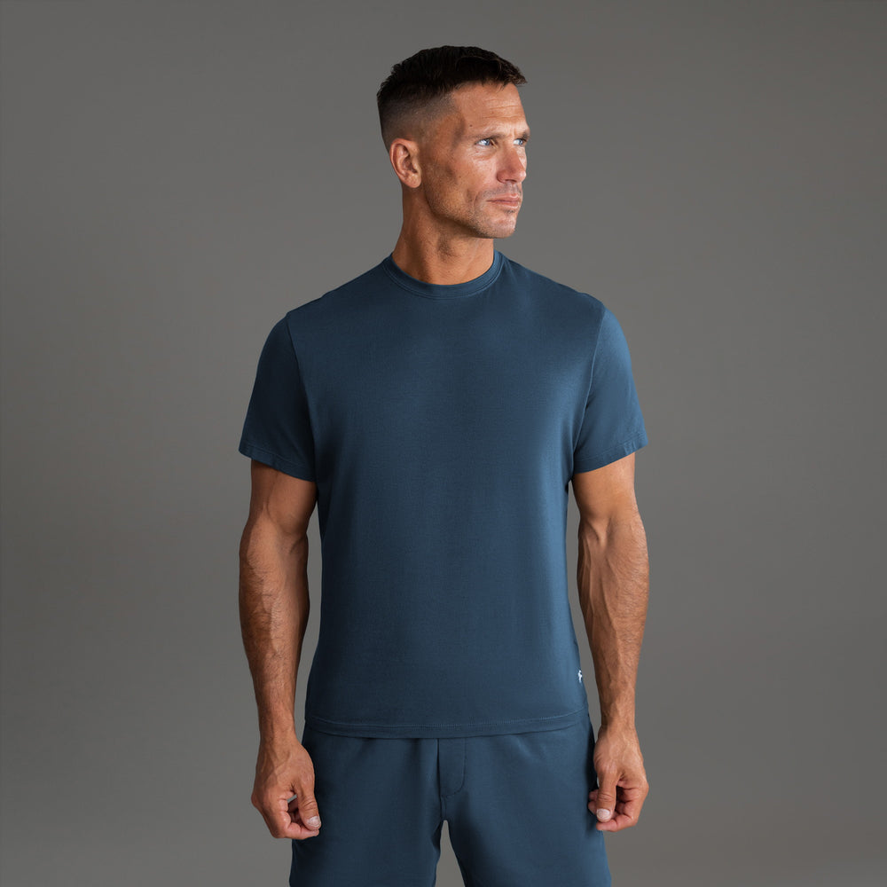 Man wearing a dark blue t-shirt and matching pants against a gray background.