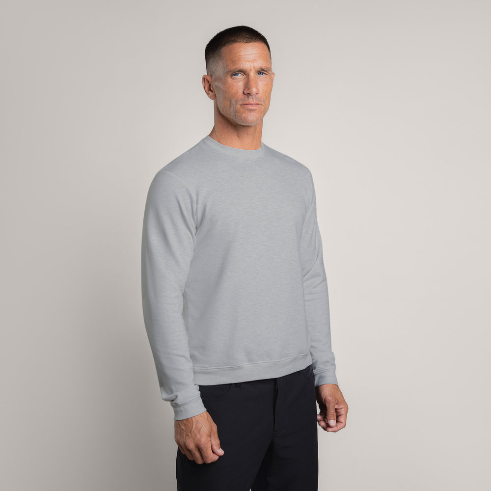 Man wearing a light gray sweatshirt and black pants against a neutral background.