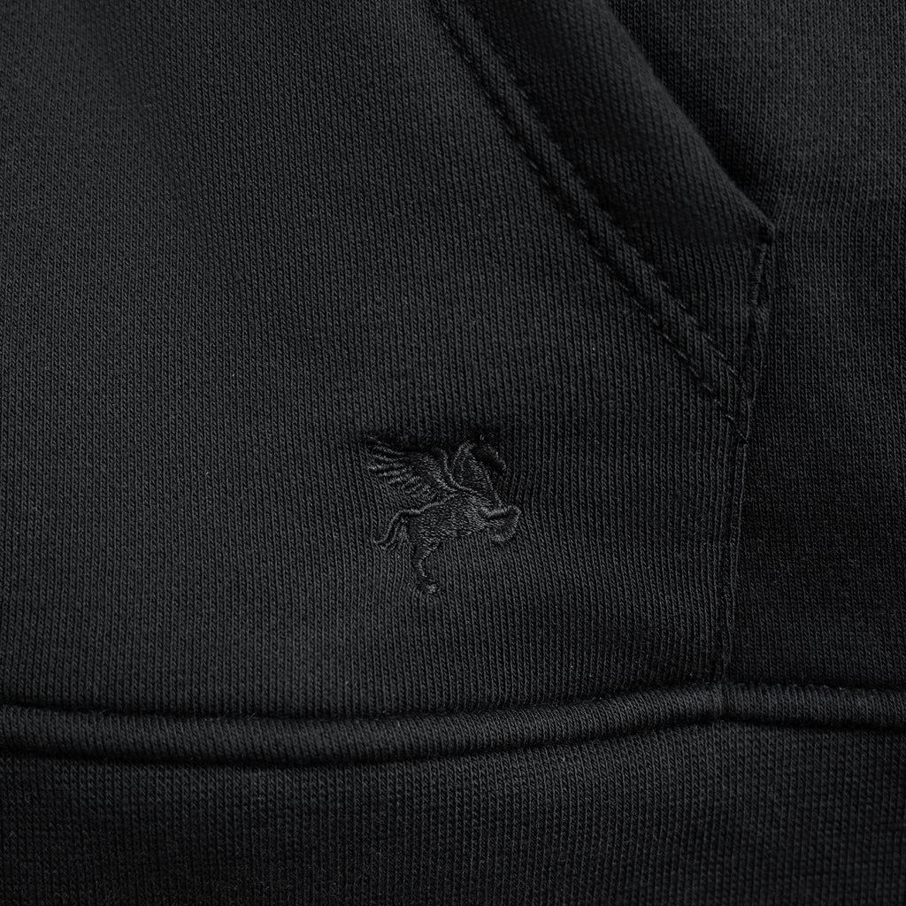 Close-up of a black jacket with a logo on the chest pocket against a black background model Kive in Black