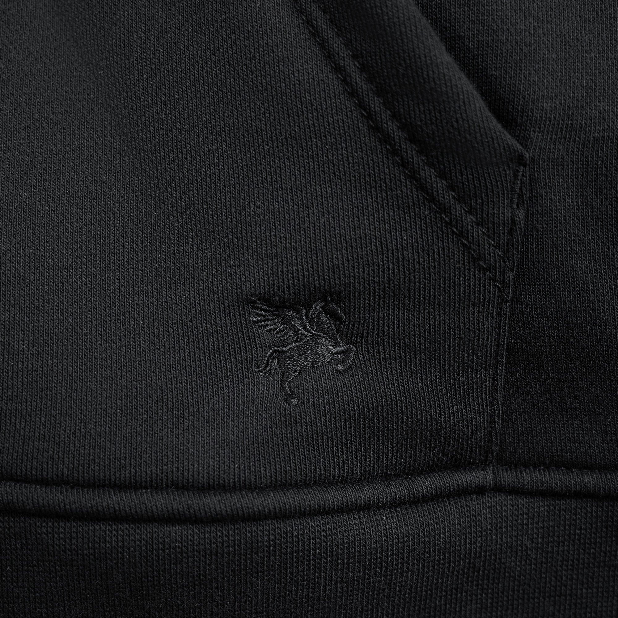 Close-up of a black jacket with a logo on the chest pocket against a black background model Kive in Black