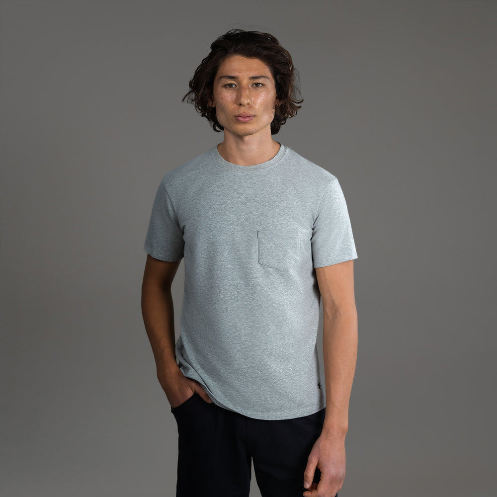 Man in gray t-shirt with hands in pockets against gray background.