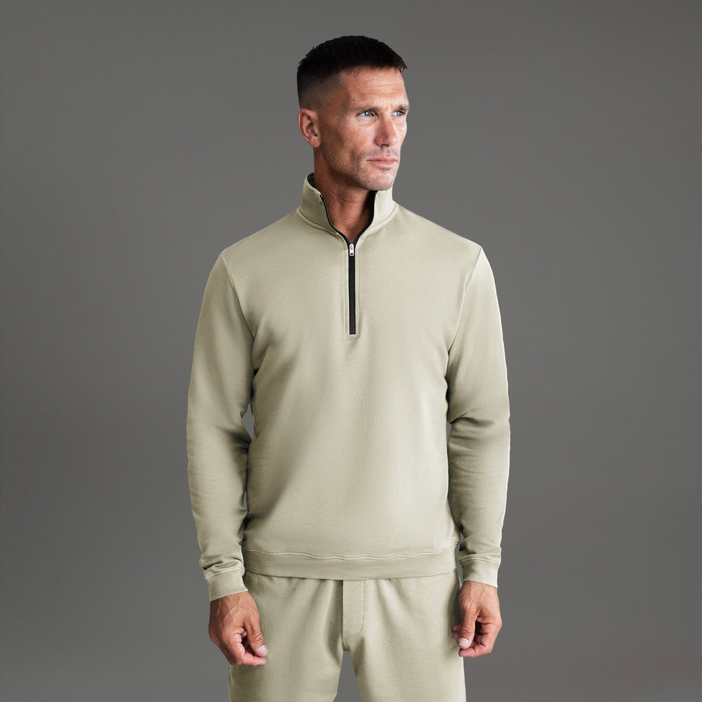 Man wearing a beige quarter-zip sweatshirt with matching pants, looking sideways against a gray background.