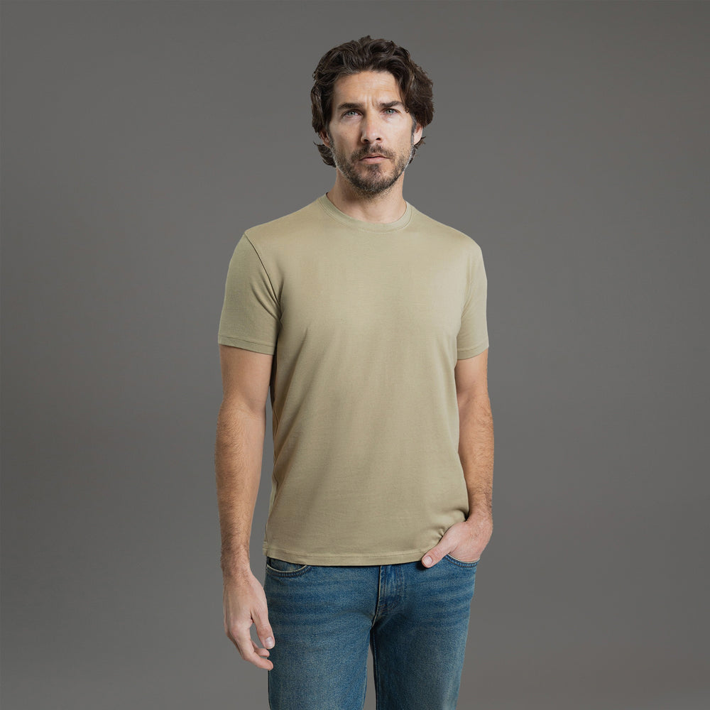 A man wearing a beige T-shirt stands against a plain gray background.
