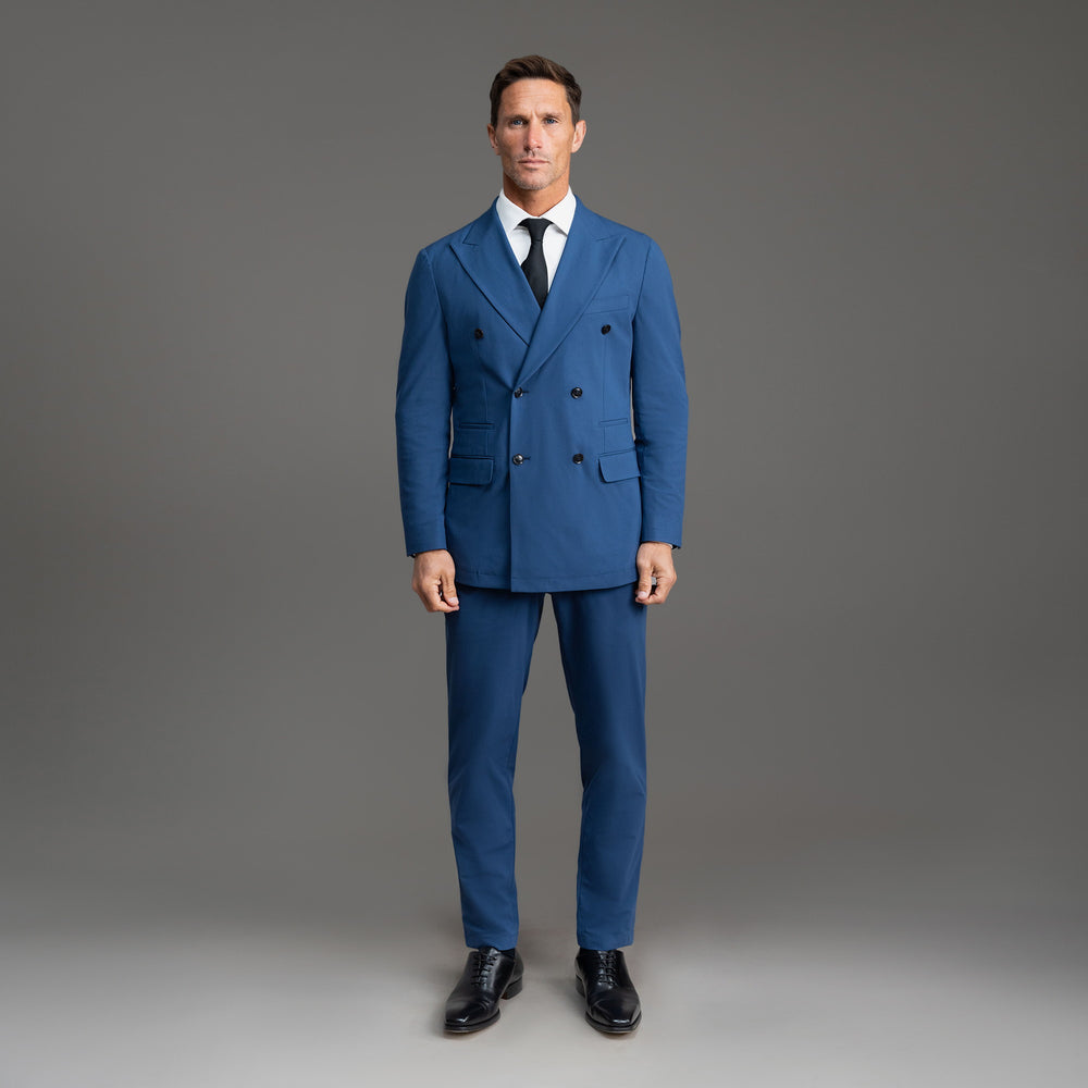 Man in a blue double-breasted suit standing against a grey background.