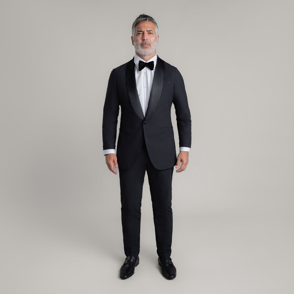 Man in a blue double-breasted suit standing against a grey background.
