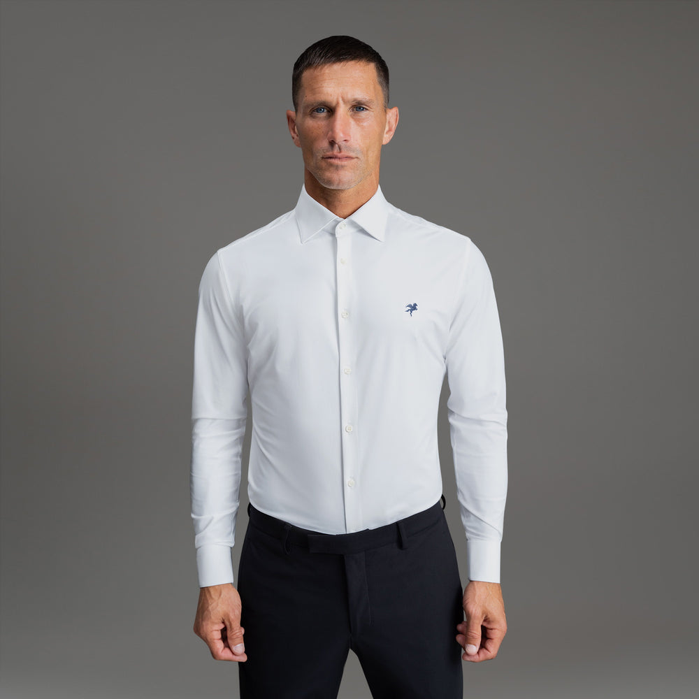 Man in a white shirt with a small logo, standing against a gray background.