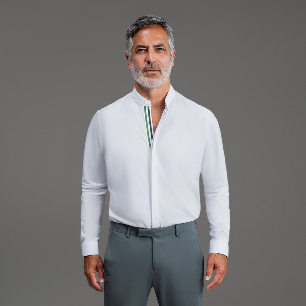 Man wearing a white shirt and gray pants standing against a gray background.