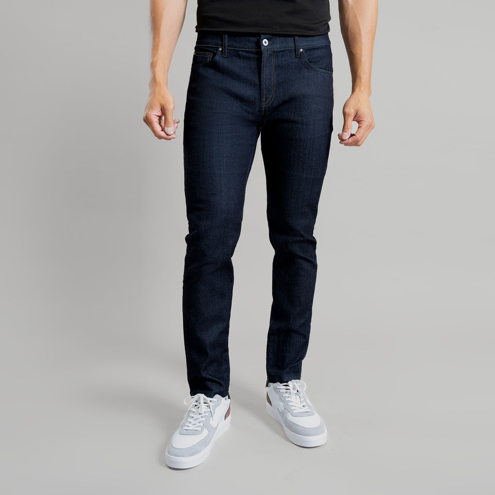 Person wearing dark blue jeans and white sneakers against a grey background.