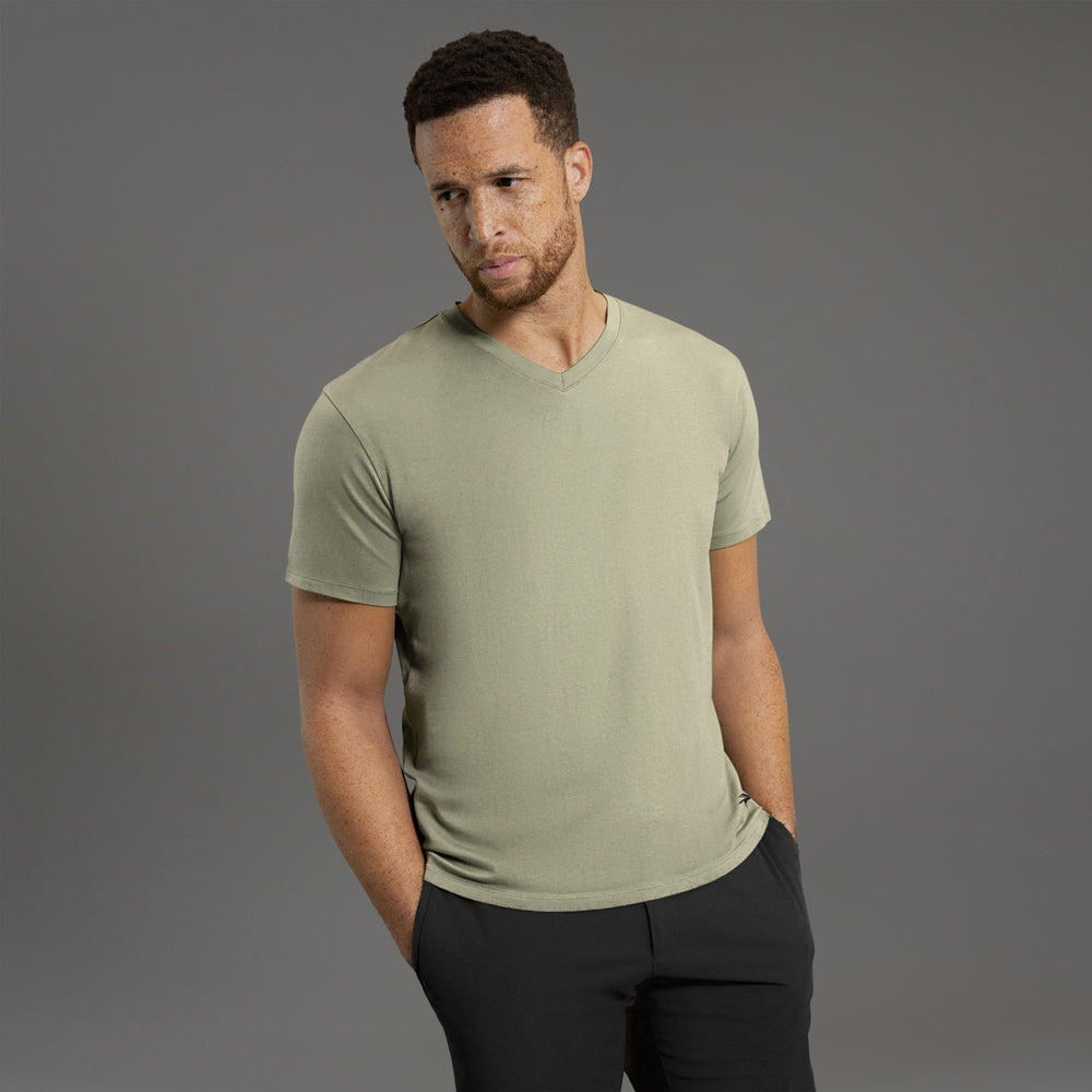 Man in a green V-neck shirt and white pants against a gray background.