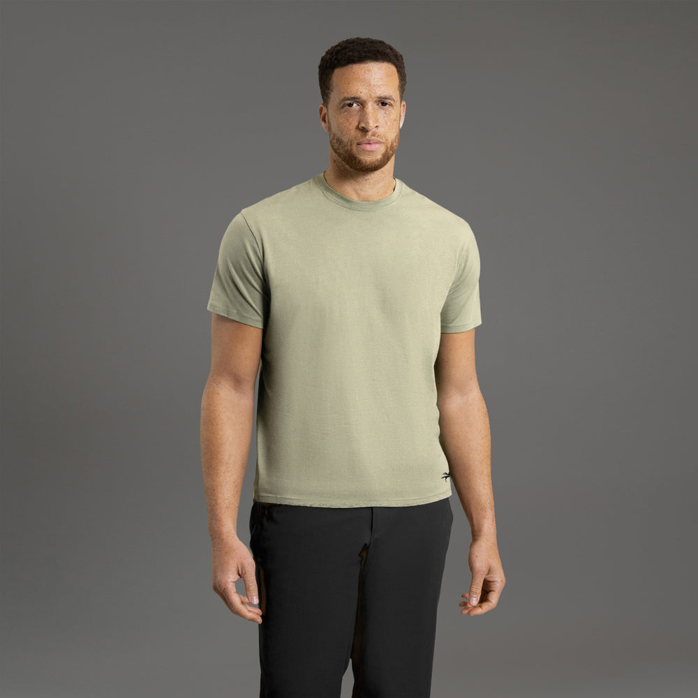Man wearing a light green t-shirt and black pants against a gray background.