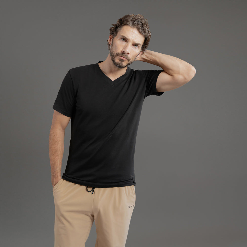 Man wearing a black V-neck t-shirt and white pants against a gray background.