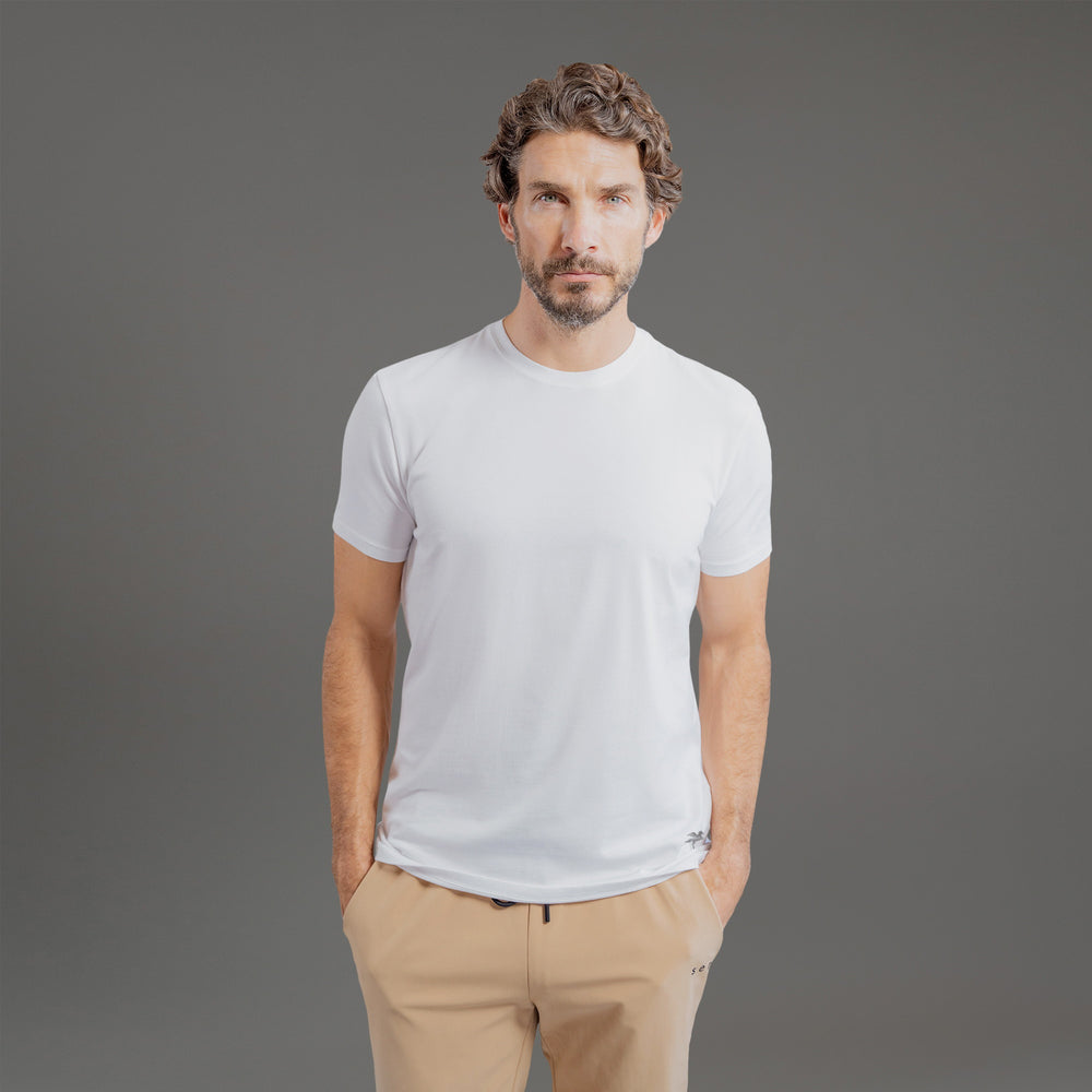 Man wearing a plain white t-shirt and beige pants, standing against a gray background.