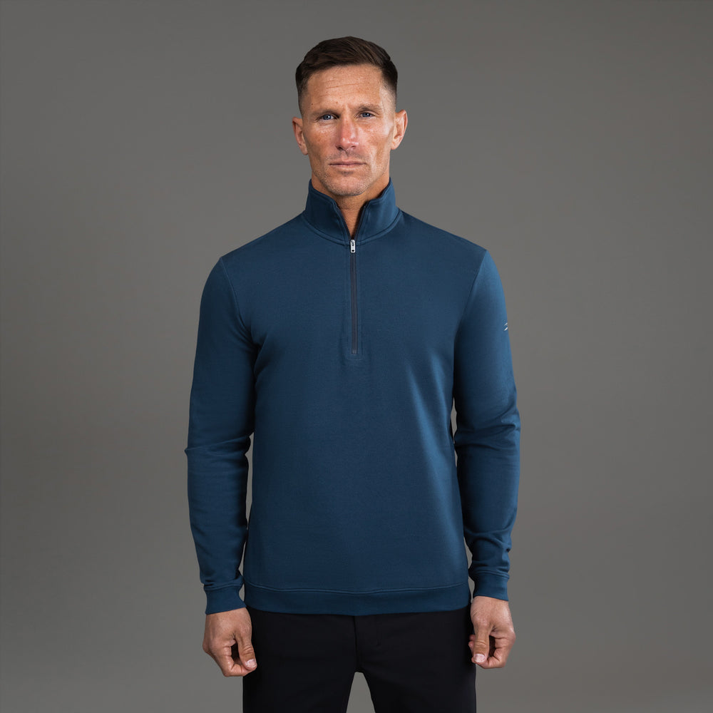 Man wearing a blue quarter-zip pullover against a gray background.