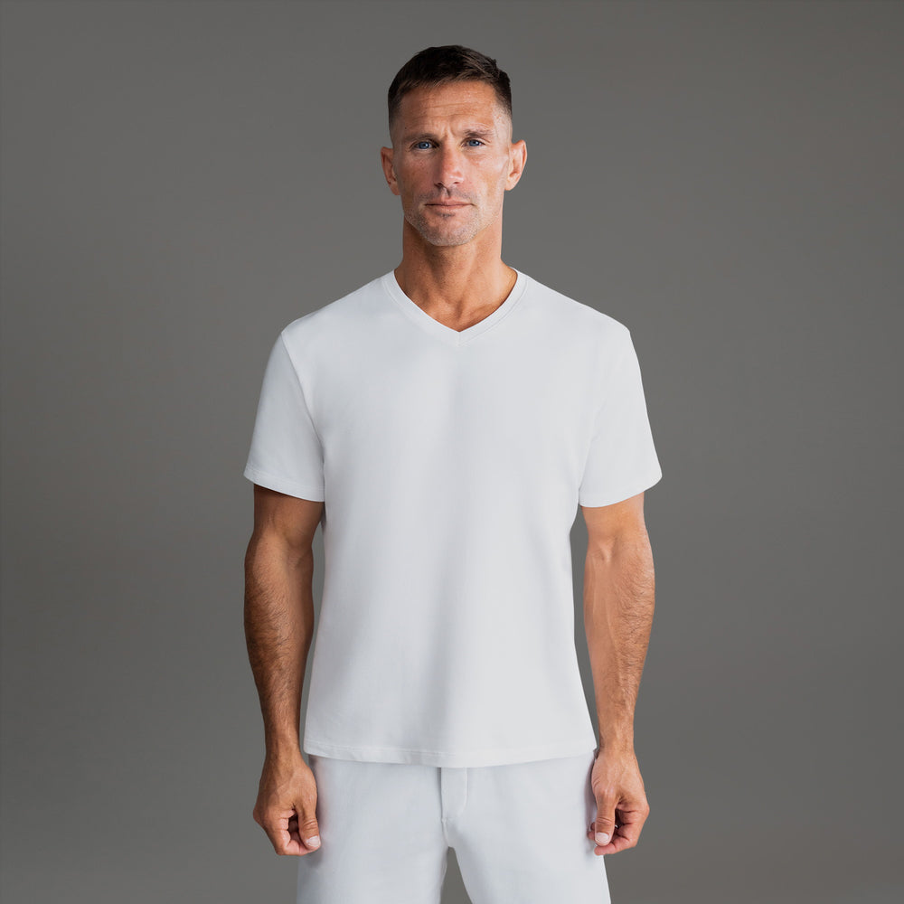 Man wearing a white V-neck T-shirt and white shorts, standing against a gray background.