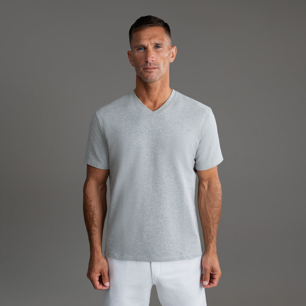 A man wearing a light gray V-neck T-shirt against a neutral background.