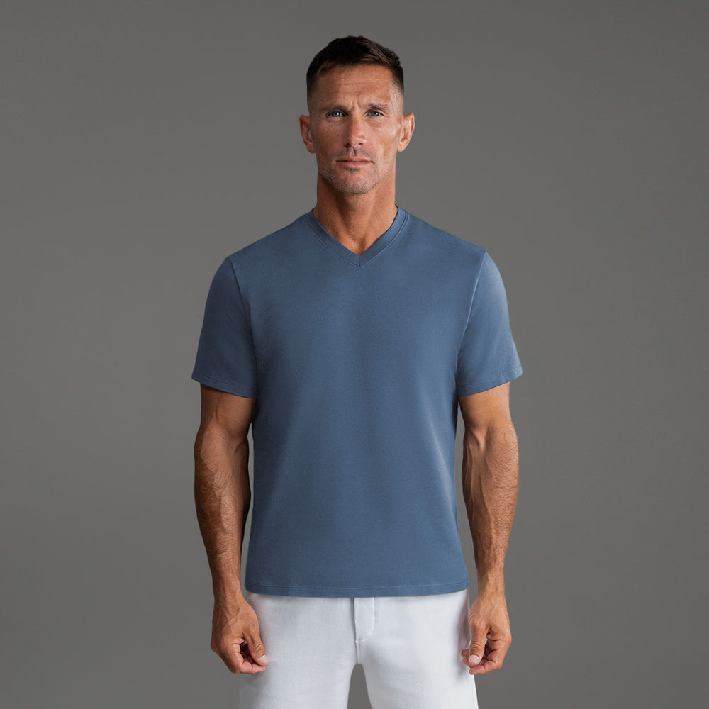 Man wearing a blue V-neck T-shirt and white pants against a gray background.