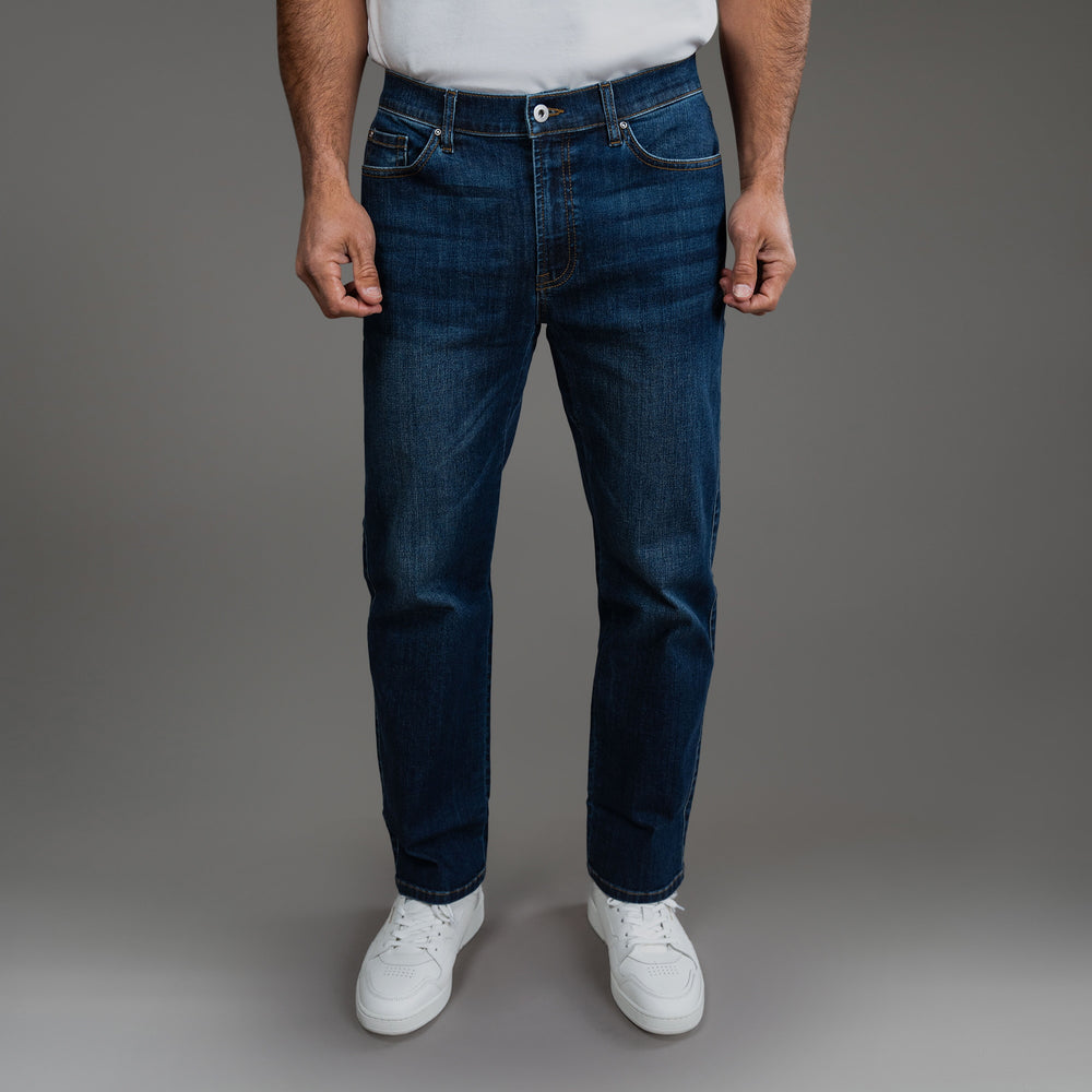 Man wearing blue jeans and white sneakers against a gray background.