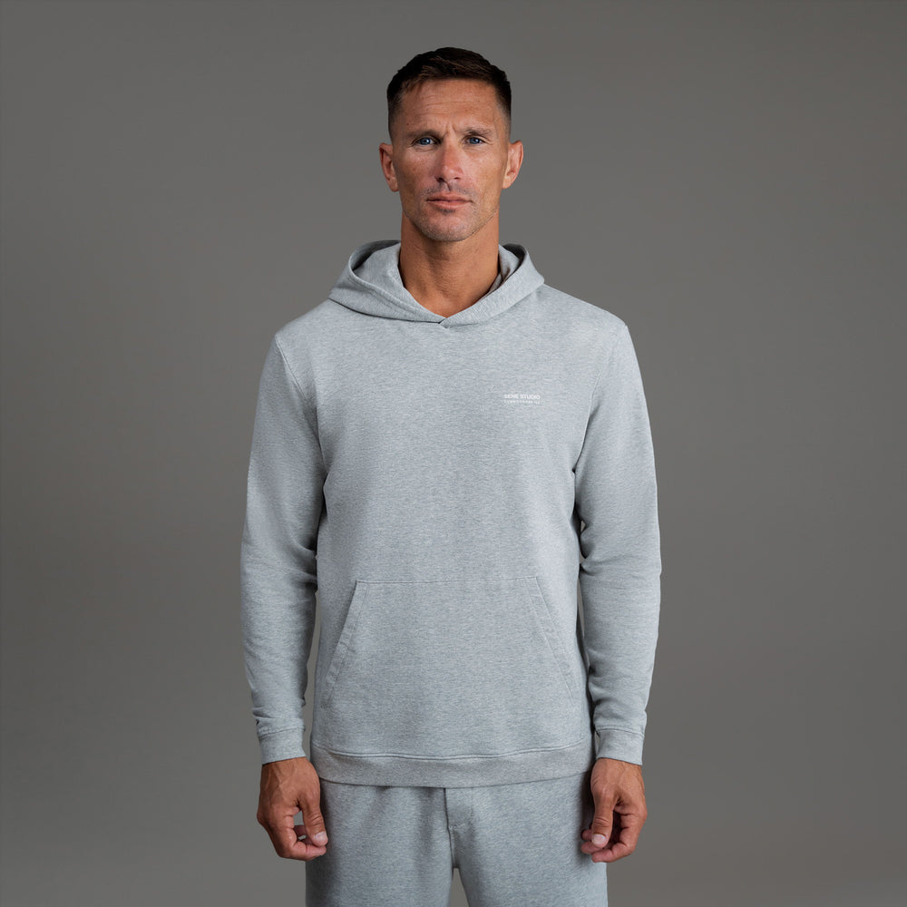 Man wearing a light gray hoodie and matching pants against a gray background.