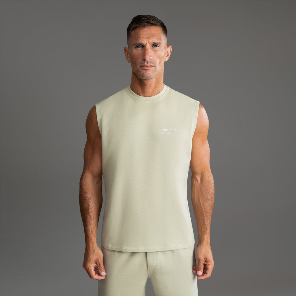 Man in sleeveless beige top and matching pants against a gray background.