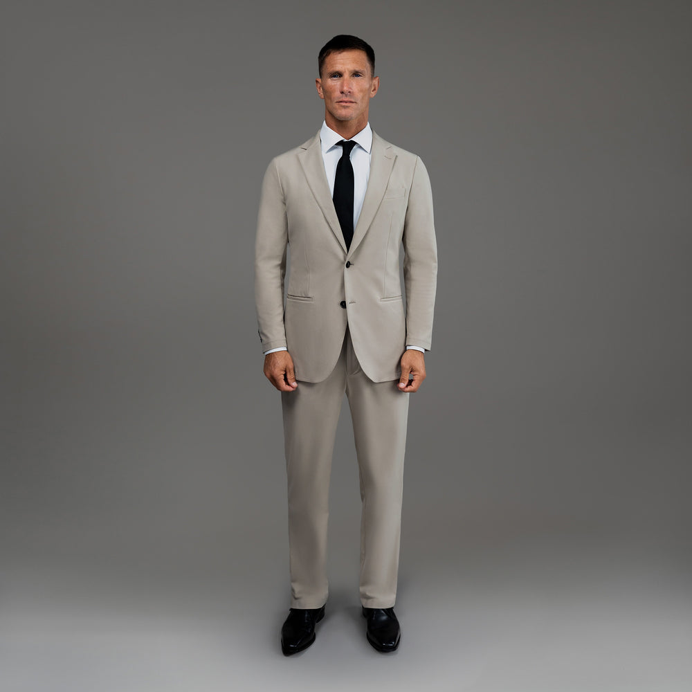 Man in a light gray suit with a black tie, standing against a gray background.