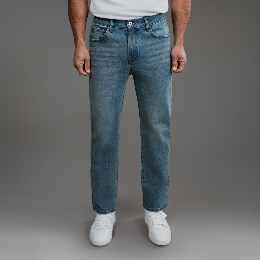 Person wearing blue jeans and white sneakers against a plain background.