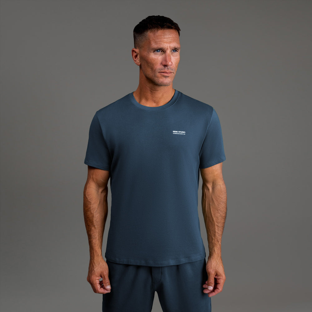 Man wearing a dark blue T-shirt and matching pants against a gray background.