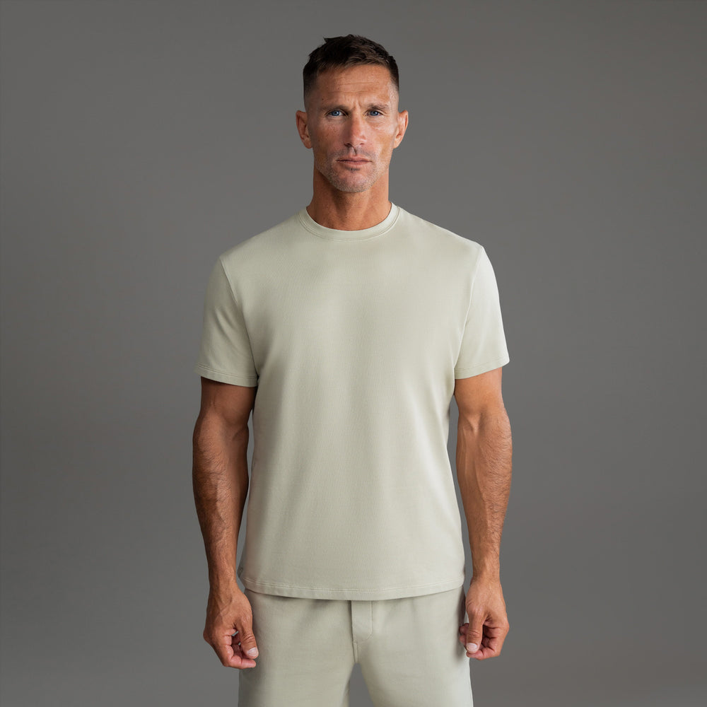 Man wearing a light beige t-shirt and matching pants against a grey background.