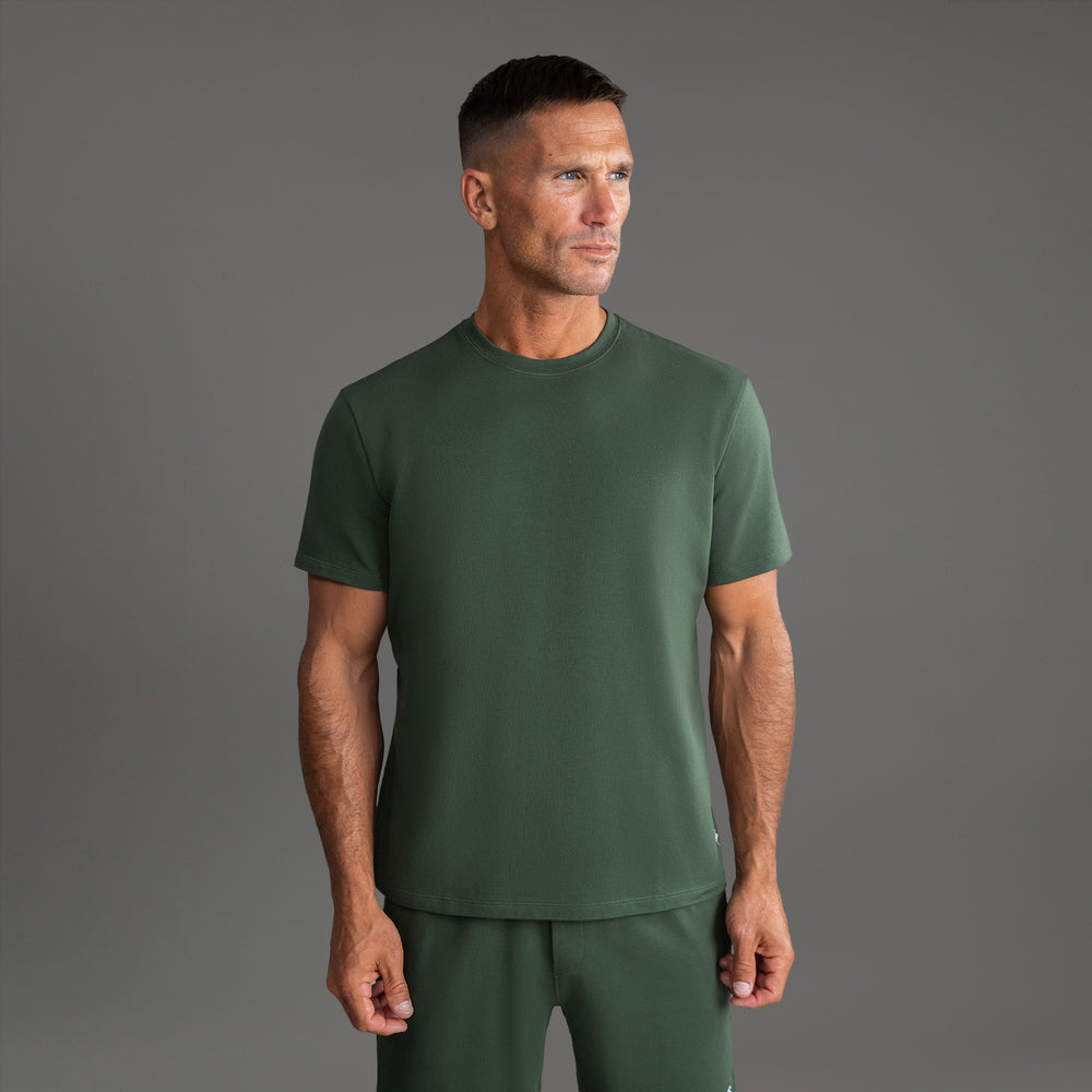 Man wearing a green t-shirt and shorts standing against a gray background.