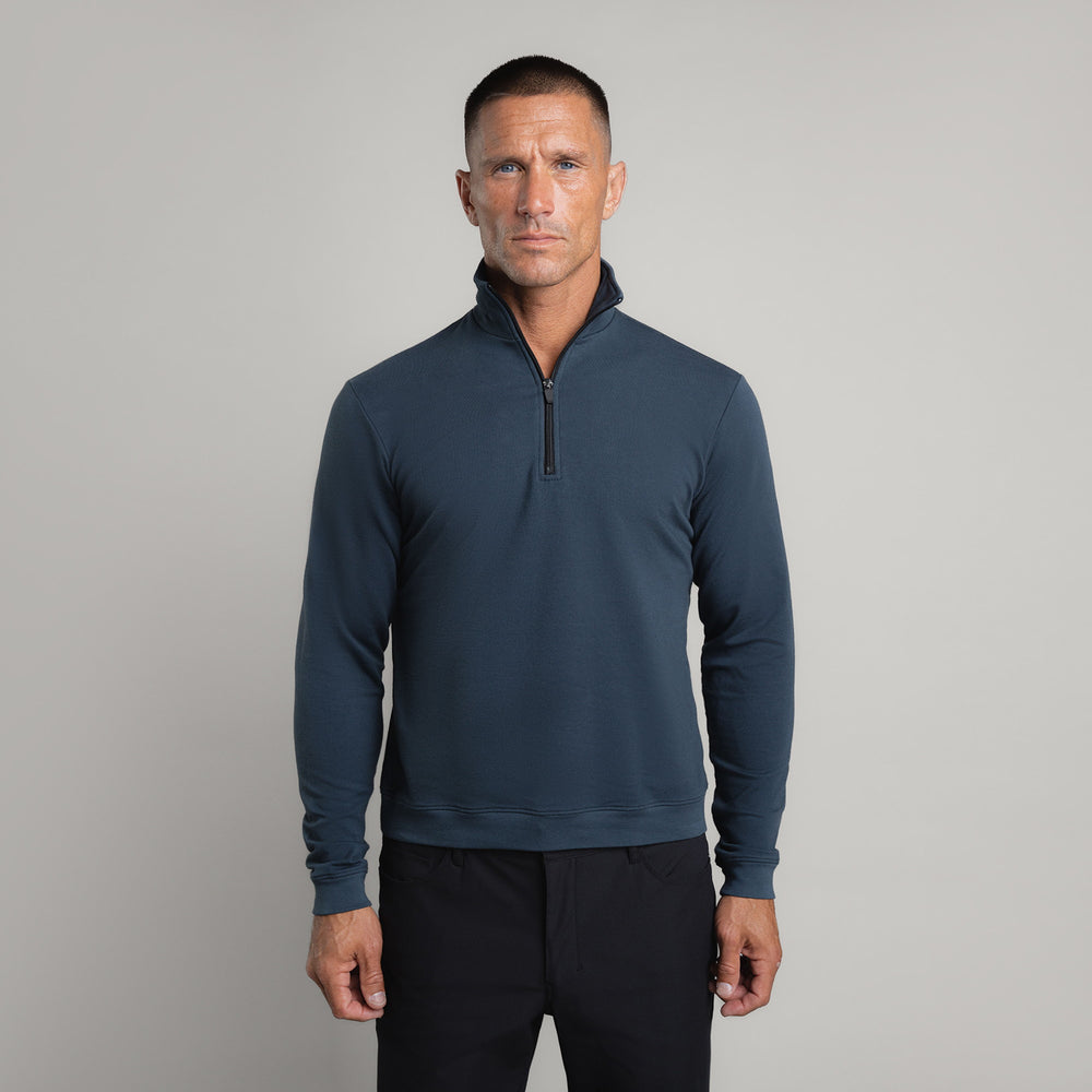Man in dark blue half-zip pullover standing against a gray background.