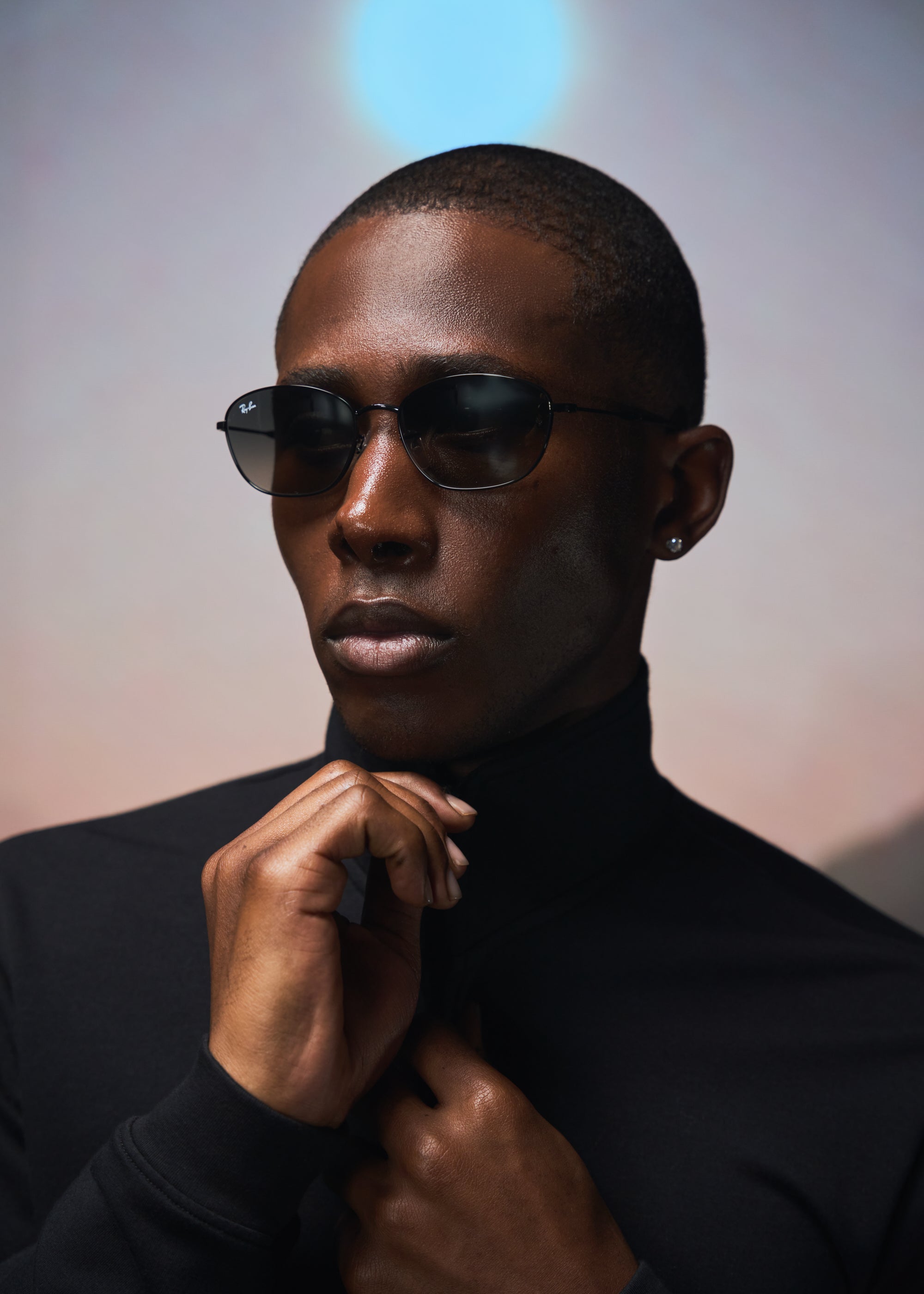 Person wearing sunglasses and a black turtleneck under soft lighting.