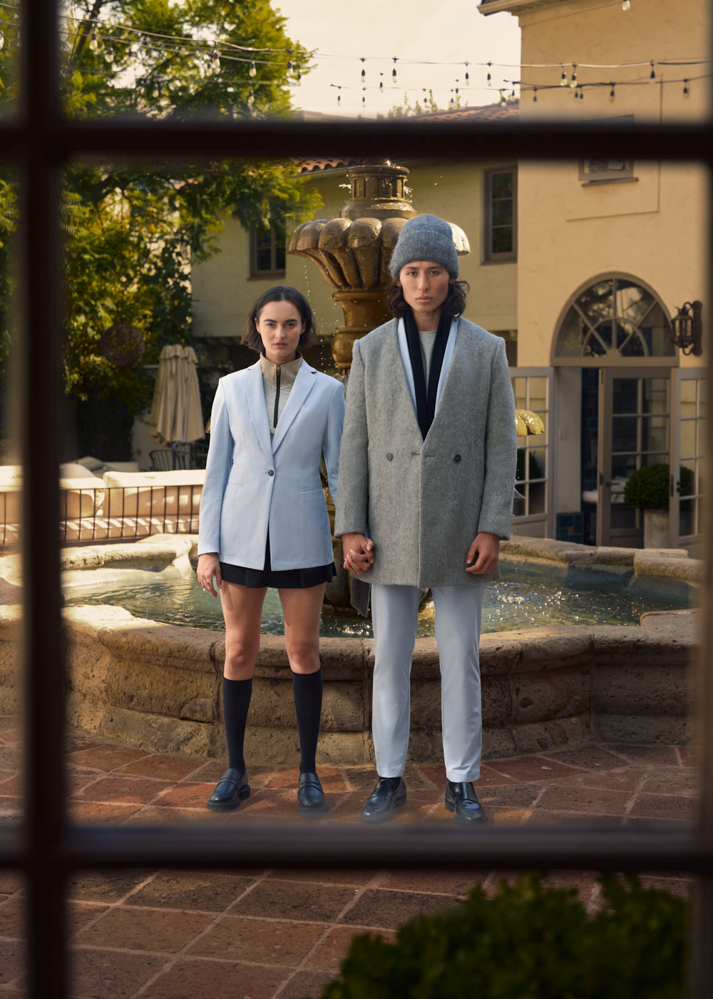 Two people in stylish outfits standing by an outdoor fountain.