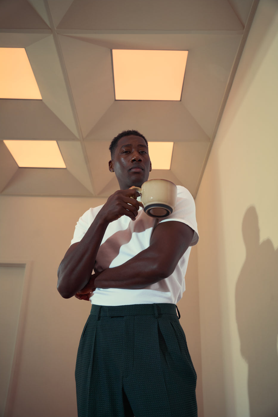 Man in a white shirt holding a large mug in a geometric ceiling room.