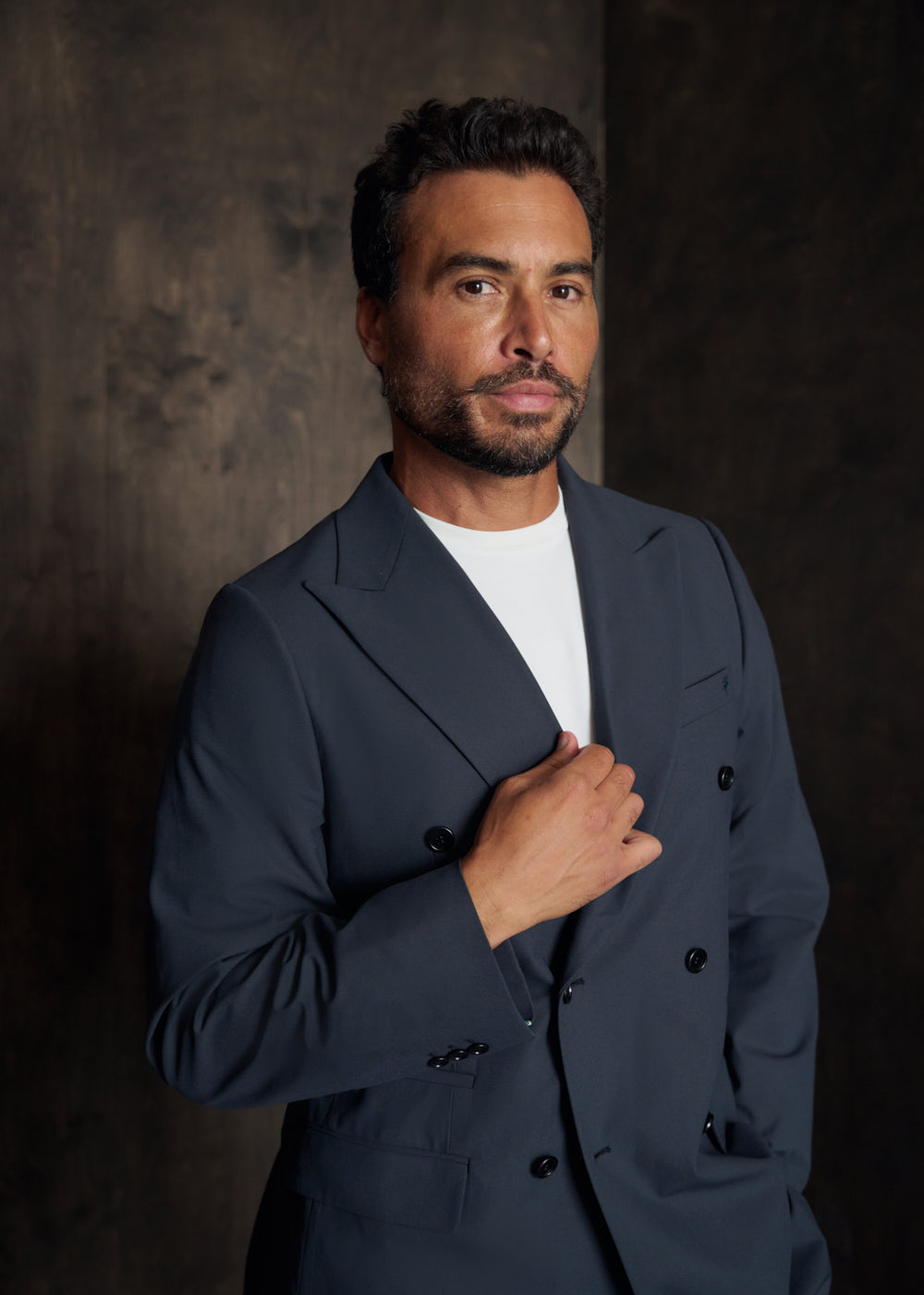 Man in a dark suit jacket posing against a dark background.