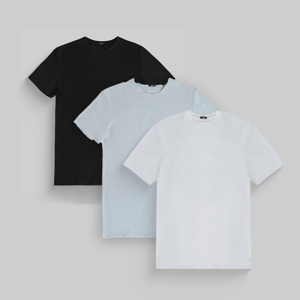 Three plain T-shirts in black, light grey, and white on a grey background.