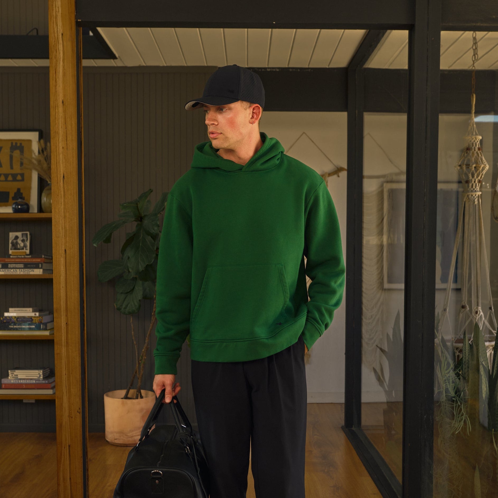 Man with hoodie holding room with wooden floors and glass walls model Tim in Eden
