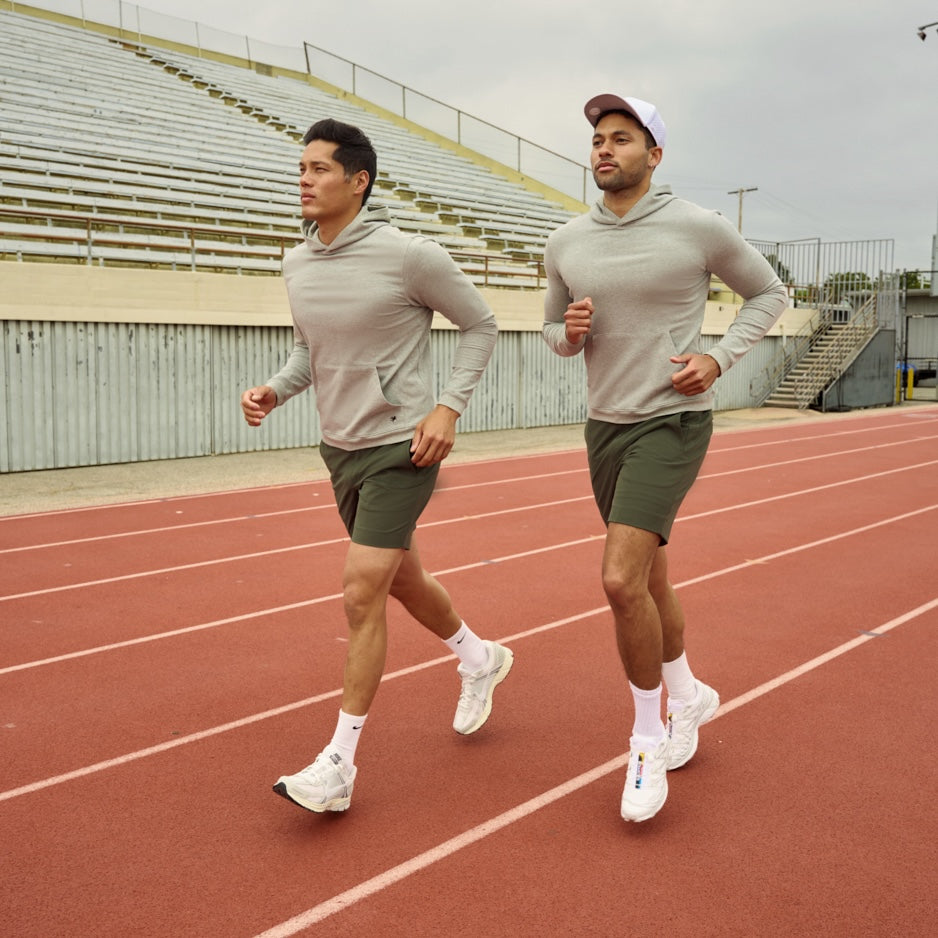 Two men jogging on a track field, wearing athletic gear.