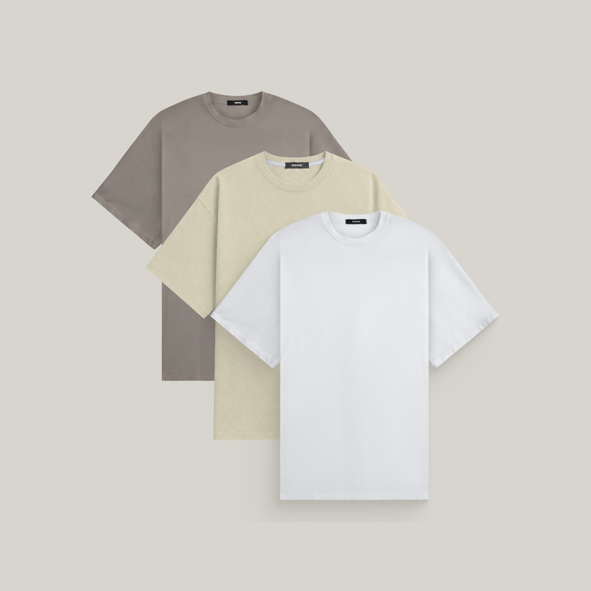 Three oversized t-shirts in frost gray, villa stone and white on a beige background model Kive in Shore