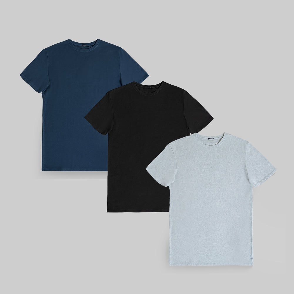 Three plain t-shirts in blue, black, and light gray displayed against a gray background.