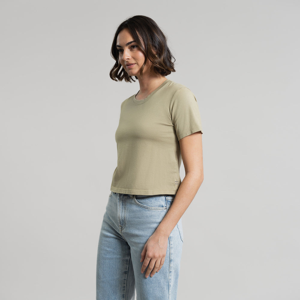 Woman in olive green t-shirt and blue jeans standing against a grey background.