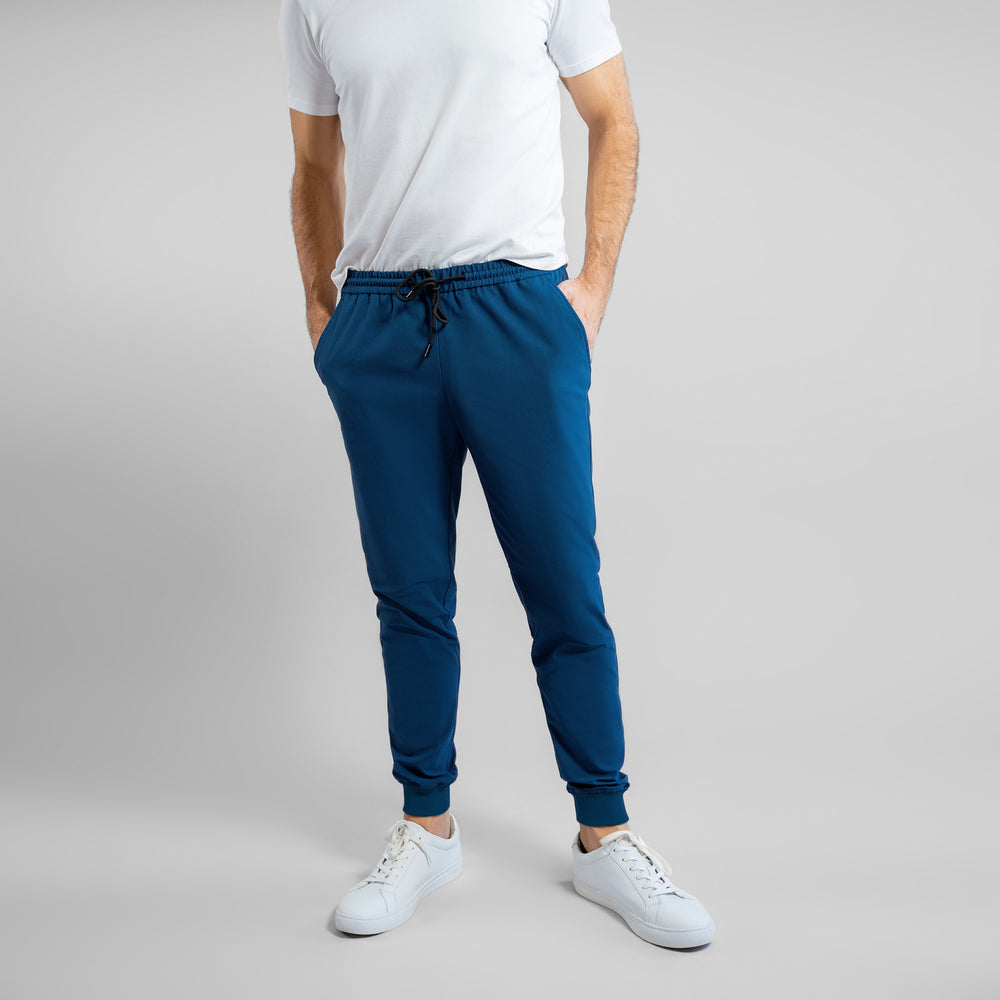 Man in white t-shirt and blue joggers against a gray background.