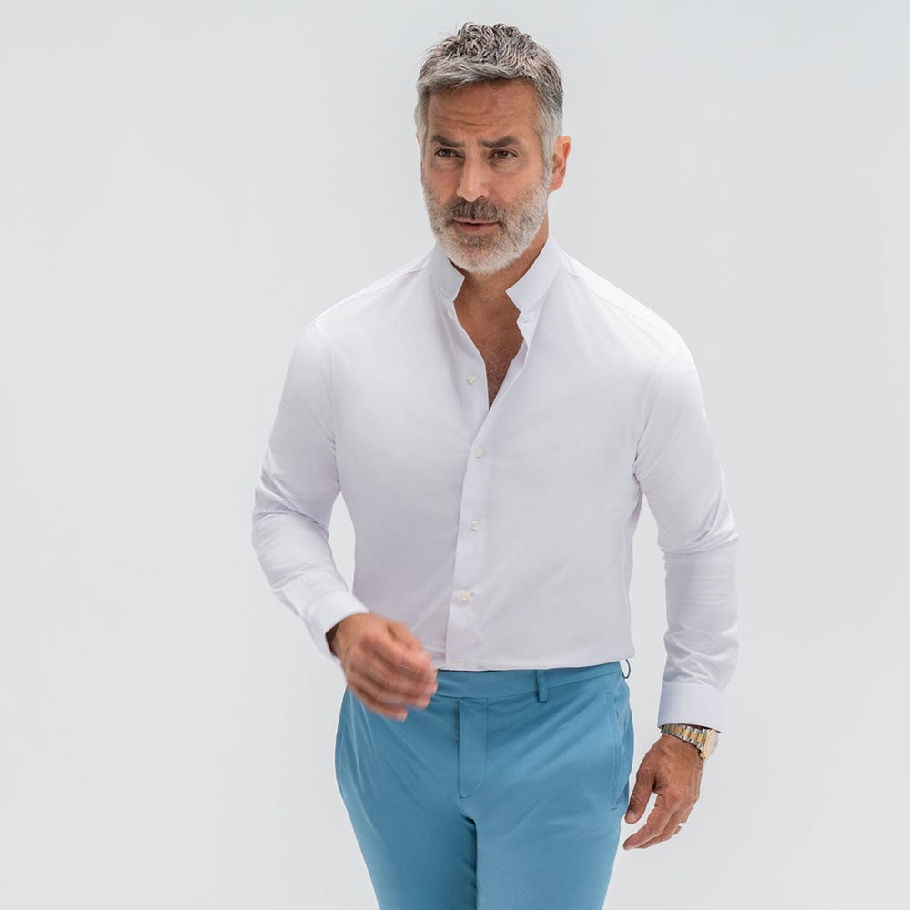 Man in a white shirt and blue pants against a plain background.